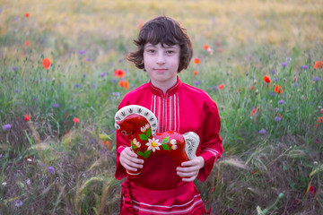 Portrait of a boy in a field with wild flowers. Boy in Russian peasant shirt. In his hands is a...