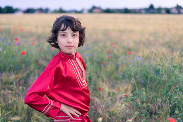 Portrait of a boy in a field with wild flowers. A boy dressed in Russian peasant shirt.