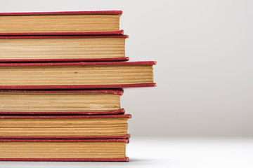 A stack of old red hardcover books with yellow pages on a white grey background.