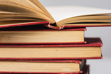 A stack of old red hardcover books with yellow pages with one open on a white grey background.