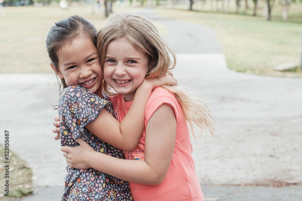 Wall mural happy and healthy mixed race multiethnic young little girls hugging and smiling in the park, best fr