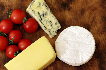 Assortment of different cheese type on a wooden board. Different pieces of cheese, blue cheese, moldy cheese, camembert and parmesan.