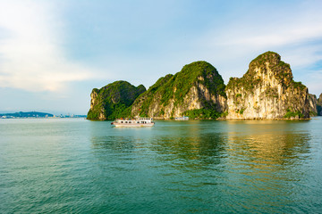 Naklejka premium Ha Long City, Vietnam - 25th June 2019: A cruise ship is sailing at sunset in Ha Long Bay, Vietnam. Beautiful sunset scenery in Ha Long Bay.