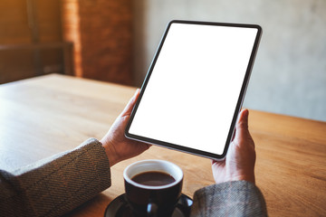Mockup image of a woman holding black tablet pc with blank white screen with coffee cup on the table