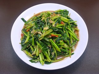 Top view of stir fried chinese kale mixed spotted mackerel in white plate on wooden table in restaurant, Healthy food concept, Ready to eat or serve