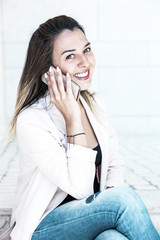 Happy beautiful customer calling on cellphone outside and smiling at camera. Joyful satisfied young woman in casual sitting outdoors and talking on phone. Mobile connection concept