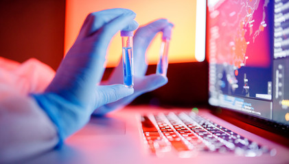 Nurse hold blood test tube in white hazmat protective suit in laboratory computer. Concept study...