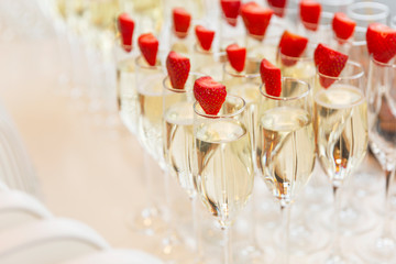 Rows of champagne glasses decorated with strawberries at the buffet table. Close-up.