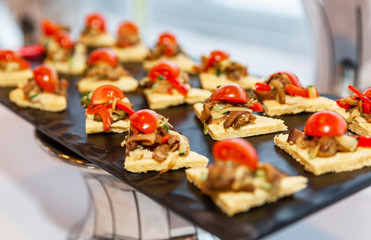 Appetizing snacks on the buffet table at the event. Canapes with meat and cherry tomatoes. Close-up.