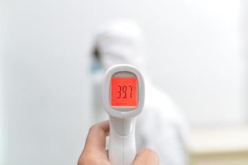 An Asian male doctor is measuring his body temperature with electronic thermometer before work to prevent the spread of the coronavirus outbreaks. The red color is high temperature, maybe he's sick