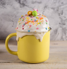 Cupcake for Easter in a mug with decoration and topping on a wooden table and a concrete background