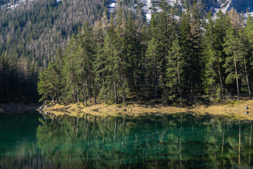 Obraz premium A view on an Alpine valley in Austria. The valley has a Green Lake in the middle. Early spring in the mountains. There is a high mountain range in the back. Freshness. Dense forest around the lake