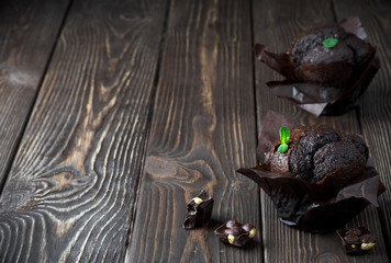 Two homemade chocolate muffin, decorated leaf mint on a dark wooden table. Near chocolate slices. Copy space, close up.
