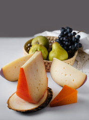 Homemade cheese slices assorted with green pears and black gape at dark background 