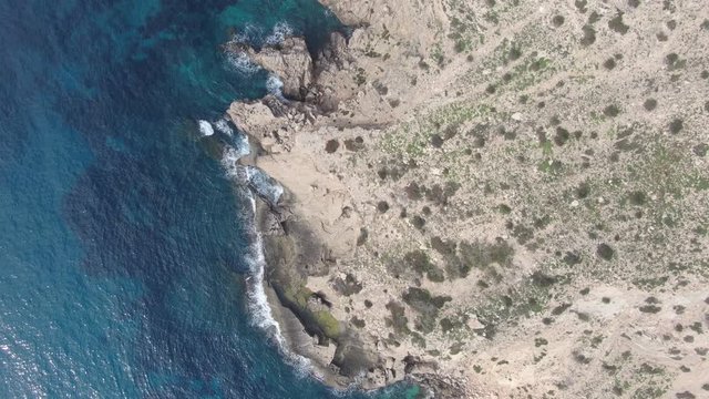 Vista a&eacute;rea con drone costa con rocas y olas rompiendo mar mediterr&aacute;neo a vista de p&aacute;jaro. Vista cenital de las olas rompiendo contra las rocas con cielo aguas cristalinas. Movimiento con drone