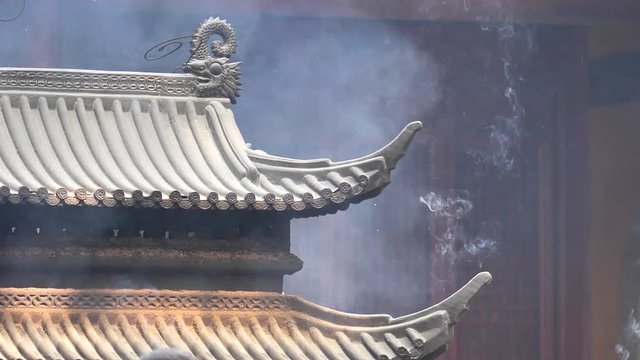 Smoke and ash raising up in the wind with traditional incense burner and temple building background, super slow motion, b roll shot.