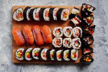 Set of homemade sushi or rolls with salmon, sesame seeds serving on a wood serving board on grey background, cooking at home.