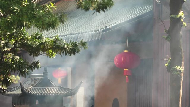 Smoke and ash raising up in the wind with traditional incense burner and temple building background, super slow motion, b roll shot.