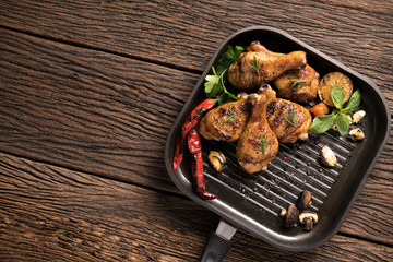 Grilled chicken leg with various vegetables on pan on old wooden background