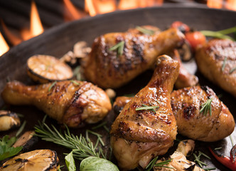 Grilled chicken leg with various vegetables on pan on the flaming grill