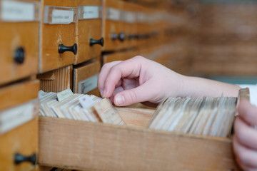 A female hand searching cards in old wooden card catalogue