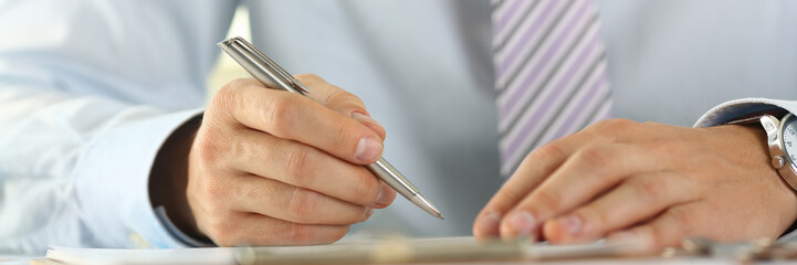 Male arm in suit and tie hold silver pen filling schedule in notepad at office workplace closeup. Legal law consult assistance gesture or finance investment advisor clerk job information gesture