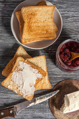 Ingredients for a delicious breakfast - toasted bread with butter and homemade raspberry jam on a wooden table