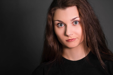 Fototapeta premium Portrait of a beautiful, young girl in black clothes with long hair. Studio photo, on a gray background. A model with clean skin.