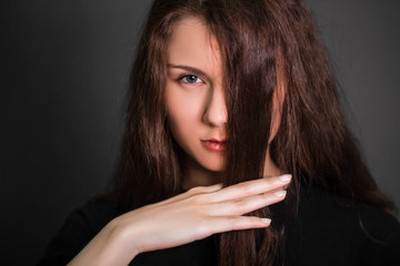 Portrait of a beautiful, young girl in black clothes with long hair. Studio photo, on a gray background. A model with clean skin.