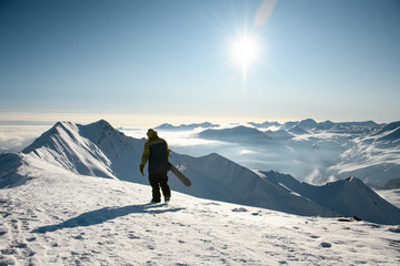 Male with snowboard walks on snowy mountain top