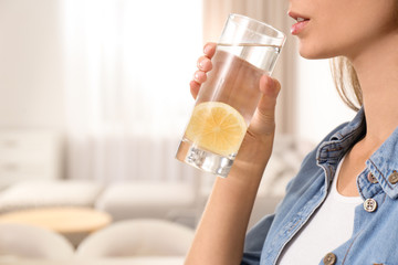 Young woman drinking lemon water at home, closeup. Space for text