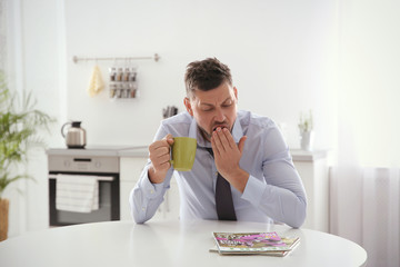 Sleepy man with cup of drink at home in morning