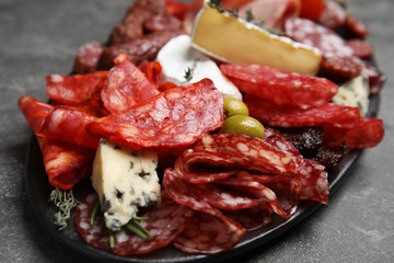 Tasty salami and other delicacies served on grey table, closeup