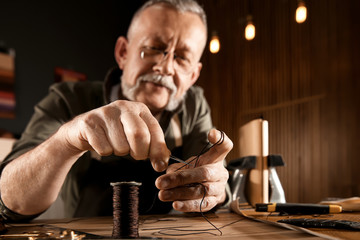 Man cutting thread while working with leather at table, focus on hands