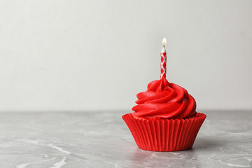 Delicious birthday cupcake with cream and burning candle on marble table. Space for text