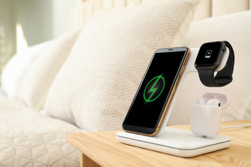 Different gadgets charging on wireless pad in bedroom. Space for text