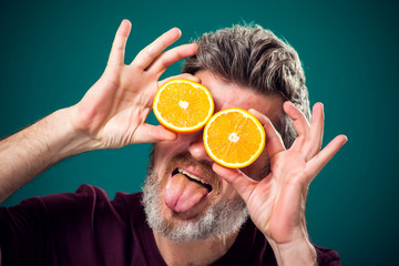 A portrait of bearded funny man holding cutted oranges behind face. People, emotions and food concept