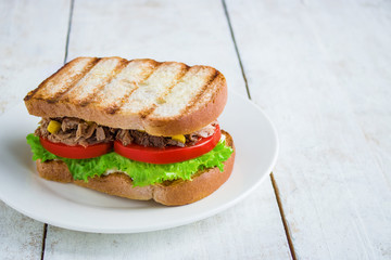 healthy tuna sandwich with grilled bread tomatoes lettuce corn onion on white plate