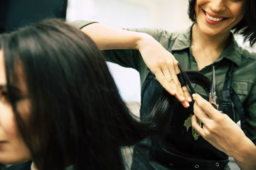 Split ends. An attractive young woman has her hair trimmed by a smiling female hairstylist.