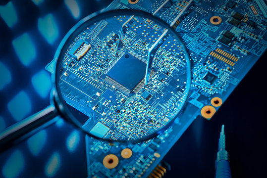 Chip on the computer's motherboard close-up through a magnifying glass. Pinch the microchip with tweezers. The concept of repair of the motherboard.