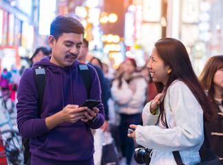 Happy Two friends asian traveler backpacker traveling in Dotonbori with neon lights at Osaka,Japan. Asian Couple using smartphone search delicious restaurants at night in light from neon billboards