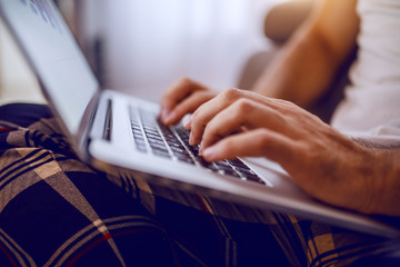 Close up of caucasian man in pajamas sitting at home and using laptop. Hands are on keyboard.