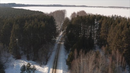 Aerial view of the road passing through the winter forest covered with ice. The road through the coniferous forest in winter. Coniferous forest in winter, shot from a quadrocopter