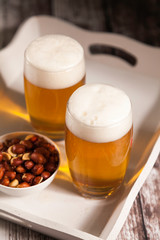 two glasses of beer with a bowl of peanuts
