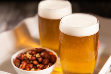 two glasses of beer with a bowl of peanuts in a tray