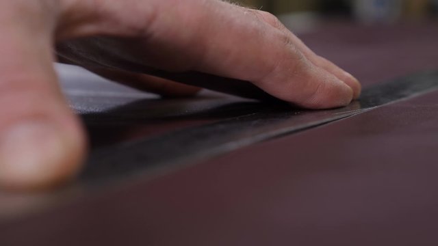 Hands of skilled leather craftsman using plastic pattern and leather knife to cut out part from piece of red leather, close-up shot. Industrial knife man cuts the work piece from the skin. 4 k footage