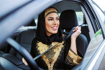 Gorgeous smiling attractive muslim woman in traditional wear sitting in her expensive car and...