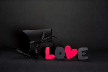 Black gift box and red word LOVE on dark background, copy space. Valentine's day, birthday romantic concept, greeting card.