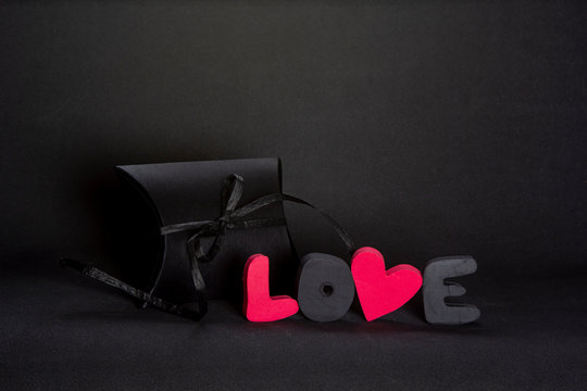 Black gift box and red word LOVE on dark background, copy space. Valentine's day, birthday romantic concept, greeting card.