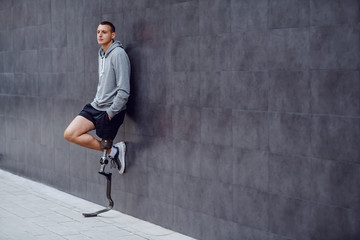 Full length of handsome caucasian sportsman with artificial leg leaning on the wall outside and...